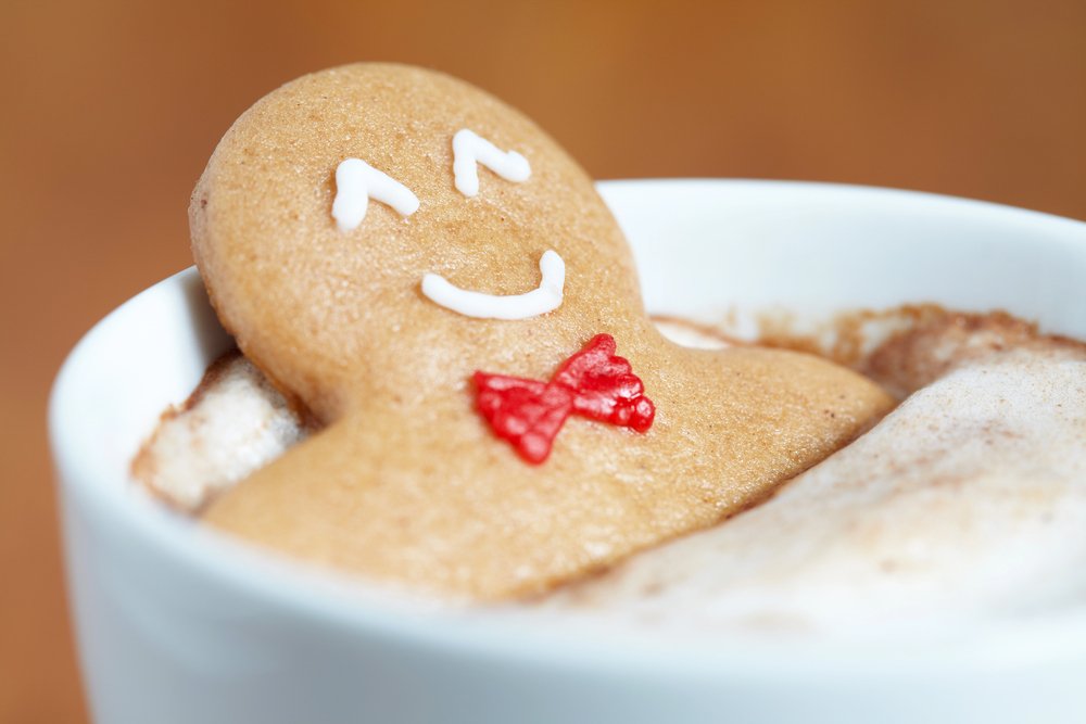 A smiling gingerbread man soaking in a cup of cocoa with foam on top